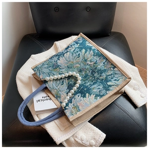 Detailed view of floral tote bag featuring pearl handle and woven strap on soft cardigan