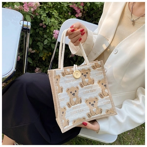 Linen tote bag detail with cartoon bear print and wood button closure in garden setting