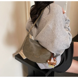 Detailed view of an olive green crescent bag featuring a teddy bear charm and textured finish