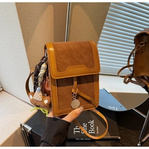 Close-up of brown PU leather crossbody bag with teddy bear pendant in natural light