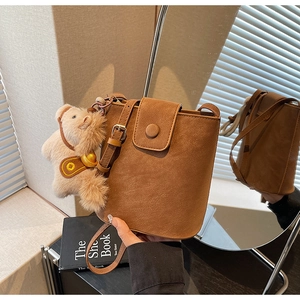 Détail du sac seau en daim marron avec breloque ours en peluche devant un miroir