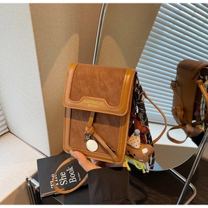 Detail of warm brown crossbody bag with flip cover and decorative bear tassel charm
