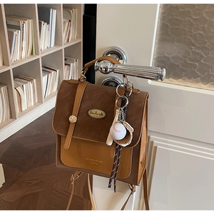 Detail van een bruine leren rugzak met 'handmade' metalen plaatje en baseball hanger