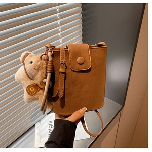 Détail d'un sac seau en daim marron avec un pendentif ours en peluche et rabat aimanté