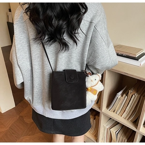 Détail d'un sac bandoulière noir mat avec un charmant pendentif chiot en peluche blanc