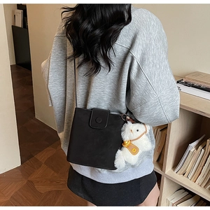 Détail d'un sac seau noir avec charme en peluche blanche sur fond d'étagère en bois
