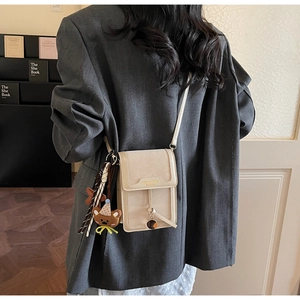 Chic beige crossbody bag with cute bear charm worn by model in a casual urban setting