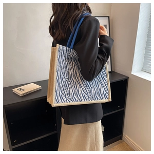 Detail of linen tote bag featuring blue zebra stripes and woven rope handle on model