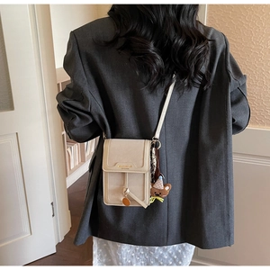 Vertical off-white crossbody phone bag with bear charm shown on grey suit blazer