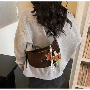Detail of a brown crescent shoulder bag with cute bear charm and silver zipper accents