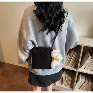 Détail d'un sac bandoulière noir mat avec un adorable pendentif en peluche d'ours