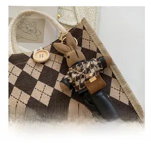 Detail view of a plush bunny keychain with houndstooth outfit on a canvas tote bag