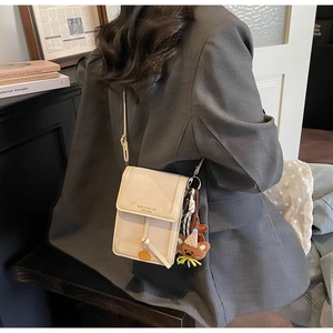 Close-up of a beige crossbody bag with a bear charm and scarf in a retro room