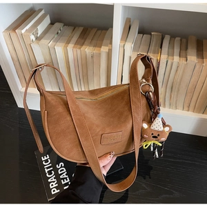 Brown moon-shaped bag with adjustable strap and cute plush bear charm on a desk