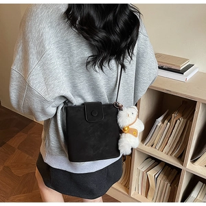 Détail d'un sac seau noir avec un charm ours en peluche blanc porté par un mannequin