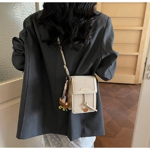 Detail view of cream crossbody phone bag with cute plush bear charm on grey blazer