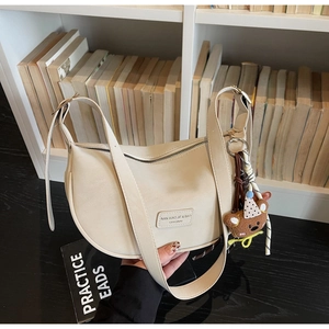 Close-up of off-white dumpling bag with adjustable strap and cute plush bear charm