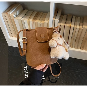 Détail d'un sac seau marron vintage avec un charm poney en peluche sur une étagère