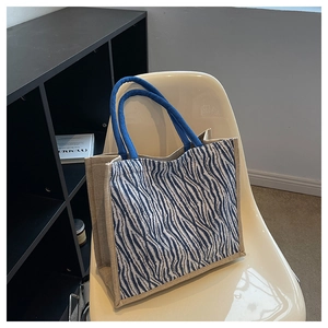 Detail of zebra-print linen tote bag with blue rope handles on a stylish chair