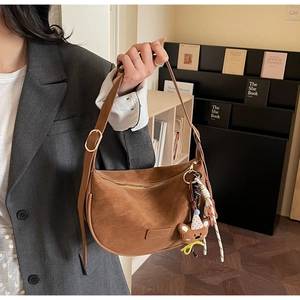 Brown suede dumpling bag with metal zipper, bear pendant, and adjustable strap detail