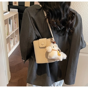 Détail d'un sac seau en cuir beige avec breloque en peluche et fermeture magnétique