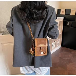 Detailed back view of a brown leather crossbody phone bag worn over a grey blazer jacket