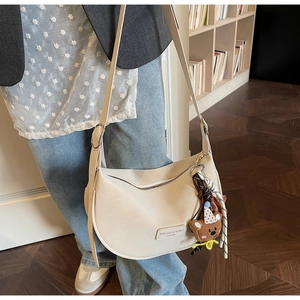 Detail of beige half-moon shoulder bag featuring a cute plush bear charm and leather logo