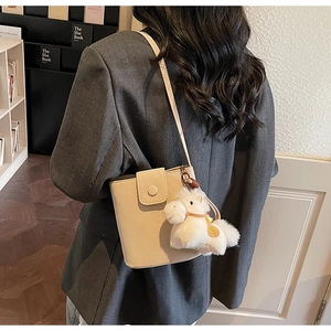 Détail d'un sac seau en cuir beige avec boucle ronde et charm poney en peluche mignon
