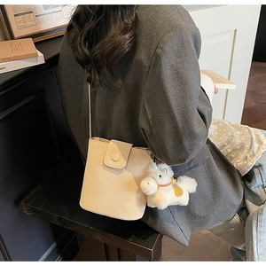 Détail d'un sac seau beige avec pendentif poney en peluche blanche et cuir mat de qualité