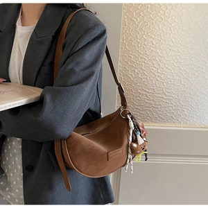 Detail of a brown suede crescent bag with adjustable strap and cute bear charm