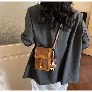 Rear view of a model wearing a brown vertical crossbody bag with a cute bear charm
