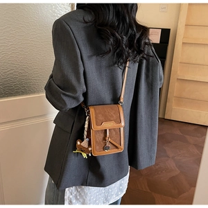 Close-up of brown faux leather crossbody bag with a cute bear charm on a female model
