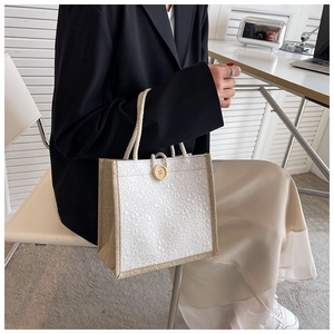 Detailed view of white textured fabric handbag with natural burlap trim and wood button