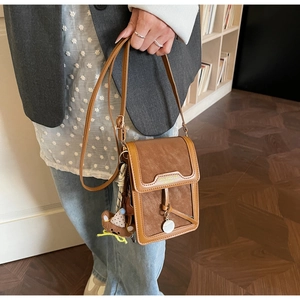 Close-up of brown crossbody phone bag with brand lettering and cute teddy bear charm