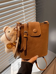Sac seau rétro marron chic avec breloque ourson présenté sur un fond de volets modernes