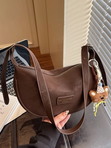 Minimalist dark brown crescent shoulder bag with plush bear charm in natural window light