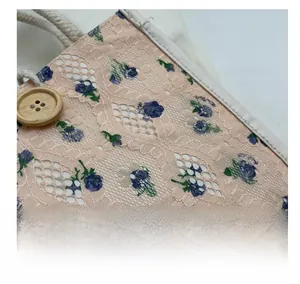 Detail of pink lace fabric with blue floral patterns, wood button, and hemp rope handle