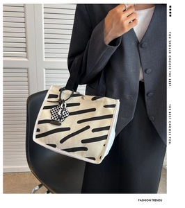Detail of canvas handbag with black stripes, checkered charm, and bicolor shoulder strap
