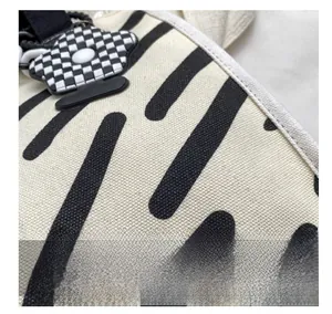 Detail einer weißen Segeltuchtasche mit schwarzen Streifen und Karoblumen-Anhänger