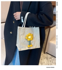 Detail of cream canvas bag with handmade yellow knitted flowers and soft white pom-poms