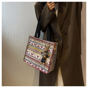 Ethnic pattern canvas tote bag with rabbit charm worn over a brown wool coat