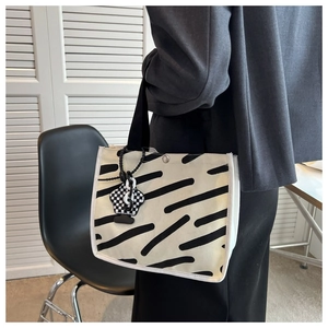 Detail of striped canvas tote bag with black strap and checkered flower charm