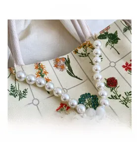 Detail showing elegant floral embroidery and luxury pearl strap on beige canvas tote bag