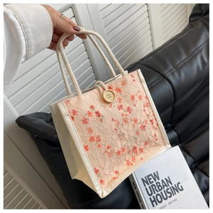 Lace canvas tote bag with floral embroidery and wooden button closure held by a hand
