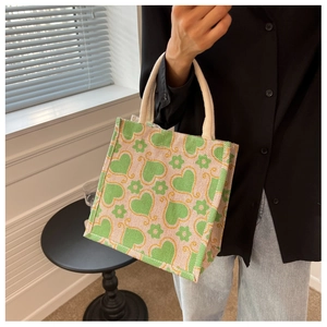 Close-up of beige linen tote bag featuring green floral heart patterns and woven handles