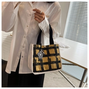 Close-up of checkered canvas handbag with floral charm and black strap detail