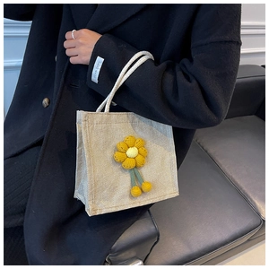 Detail of beige linen tote bag featuring handmade yellow crochet flowers and rope handles