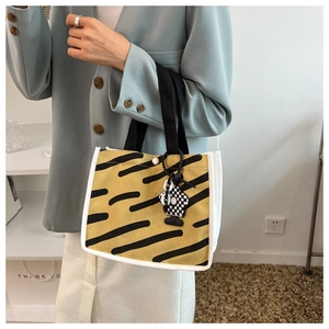 Detail of yellow canvas tote with black tiger stripes and checkered cartoon charm
