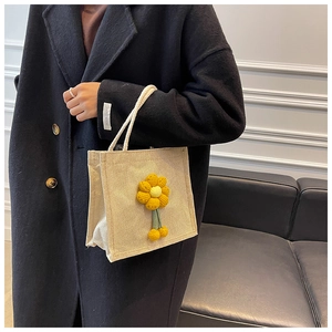 Detail of beige linen tote bag featuring a yellow crochet flower and white cord handle