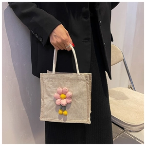 Close-up of white canvas handbag featuring a pink crochet flower and yellow charms